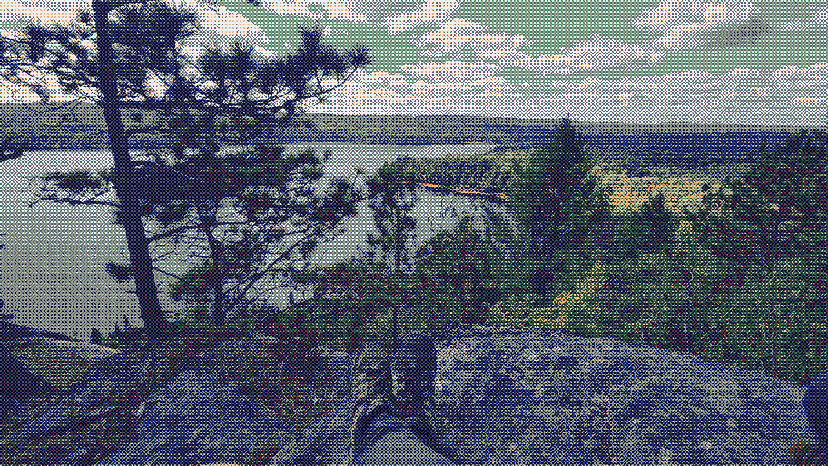 A lookout from a ridge over a blue lake, surrounded by green forest.